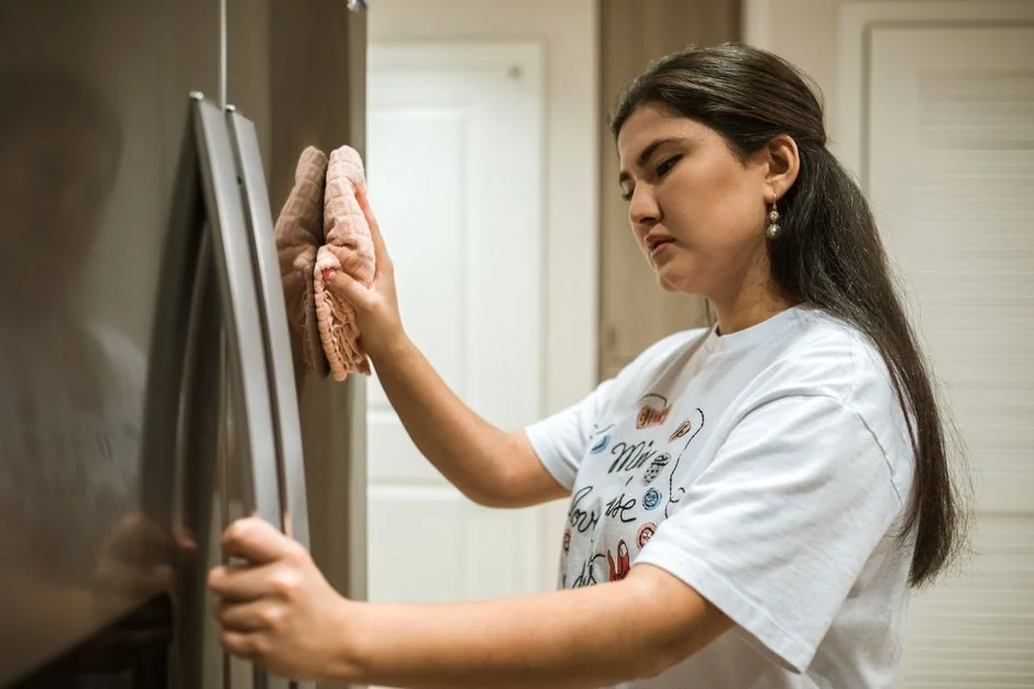 A woman cleans a mirror indoors using a blue cloth, reflecting cleanliness and home care.